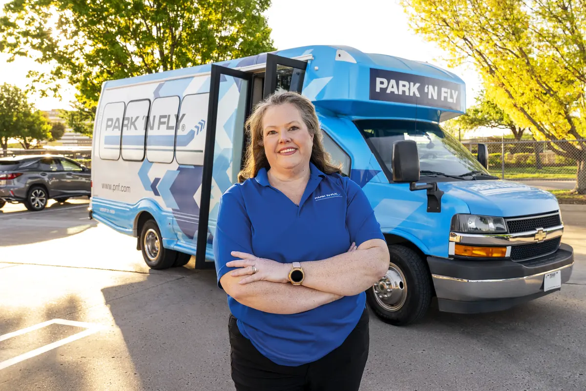 A Park N Fly shuttle driver in front of the blue the Park N Fly airport shuttle