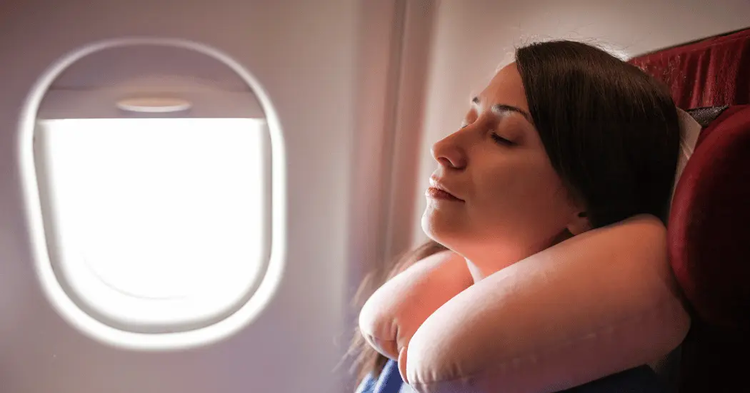 An economy rate passenger rests with a neck pillow